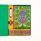 Colorful Frida Kahlo stationery gift set arranged inside a green box on a white background. The set includes a decorative notebook with Frida Kahlo's artwork, several matching patterned pencils, a white sharpener with a floral and vine illustration, and a pink point guard.