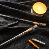 Two Blackwing Gift Card Pencils and a candle are displayed on a black cloth.