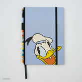 A light blue hardcover notebook featuring Donald Duck's face on the cover, with a black elastic closure band and a matching black ribbon bookmark. A matching colorblock pencil with colorful Donald Duck illustrations is tucked into the left side of the notebook.