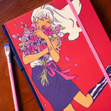 A red Blackwing Artist Series Slate Notebook - Leslie Hung with a cartoon of a woman holding flowers, and a Blackwing pencil.