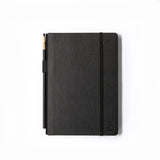 A Medium Blackwing Slate Notebook with lay-flat binding and a pen on a white surface.