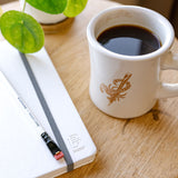 A mug of Blackwing x Timeless Coffee Bundle next to a notebook.