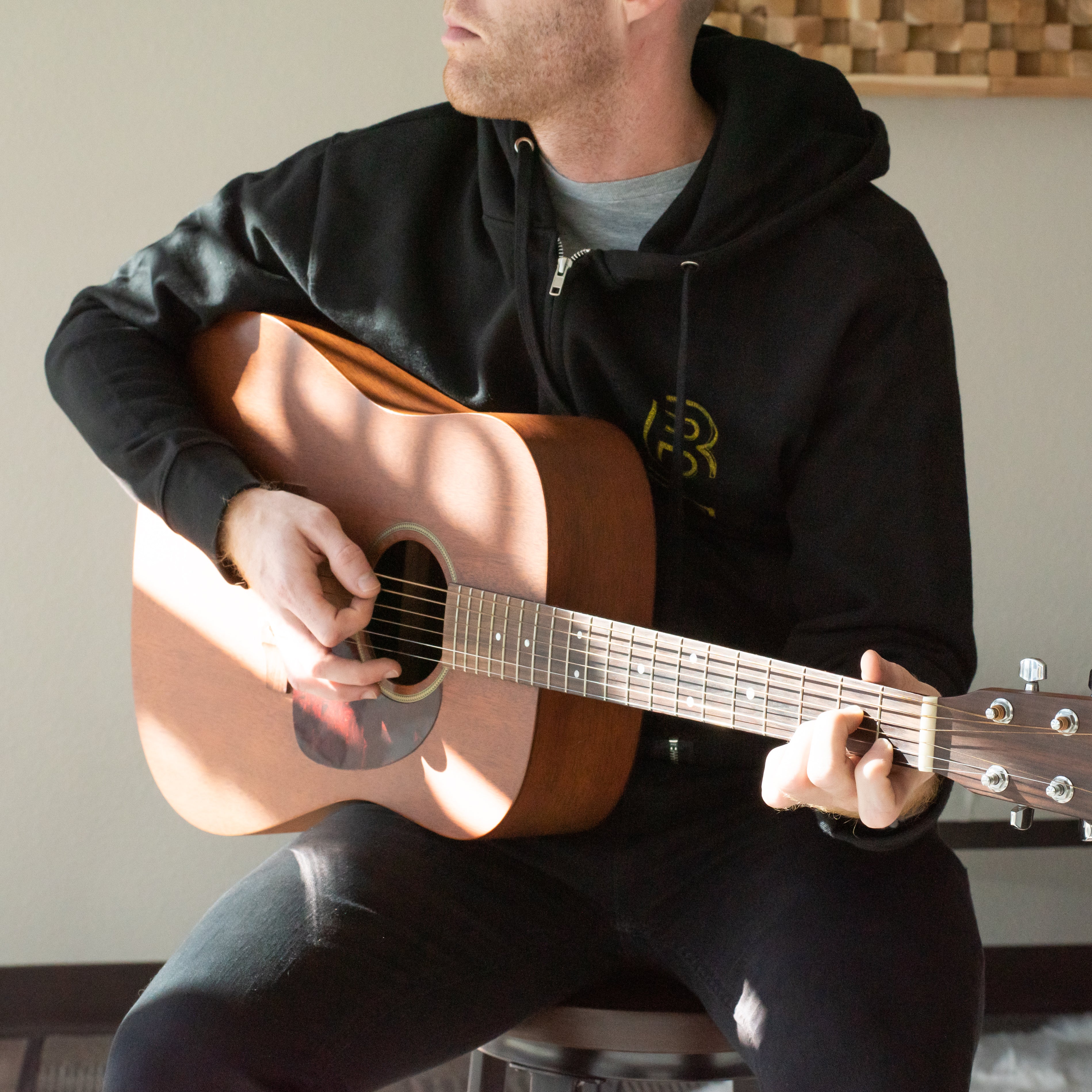 A man in a Blackwing Sketch Zip-up Hooded Sweatshirt strums an acoustic guitar.
