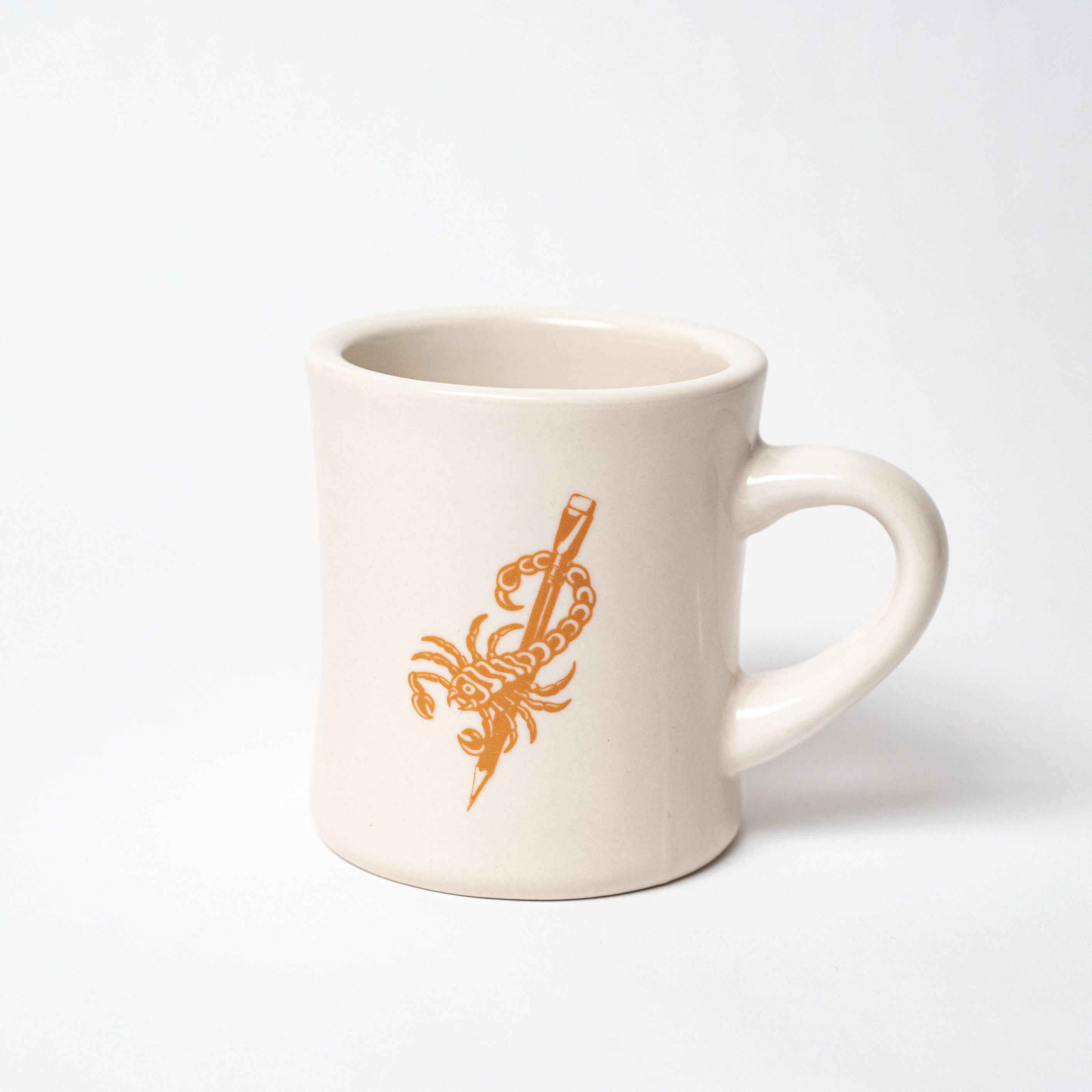 A white mug with an orange Blackwing x Timeless Coffee Bundle design.