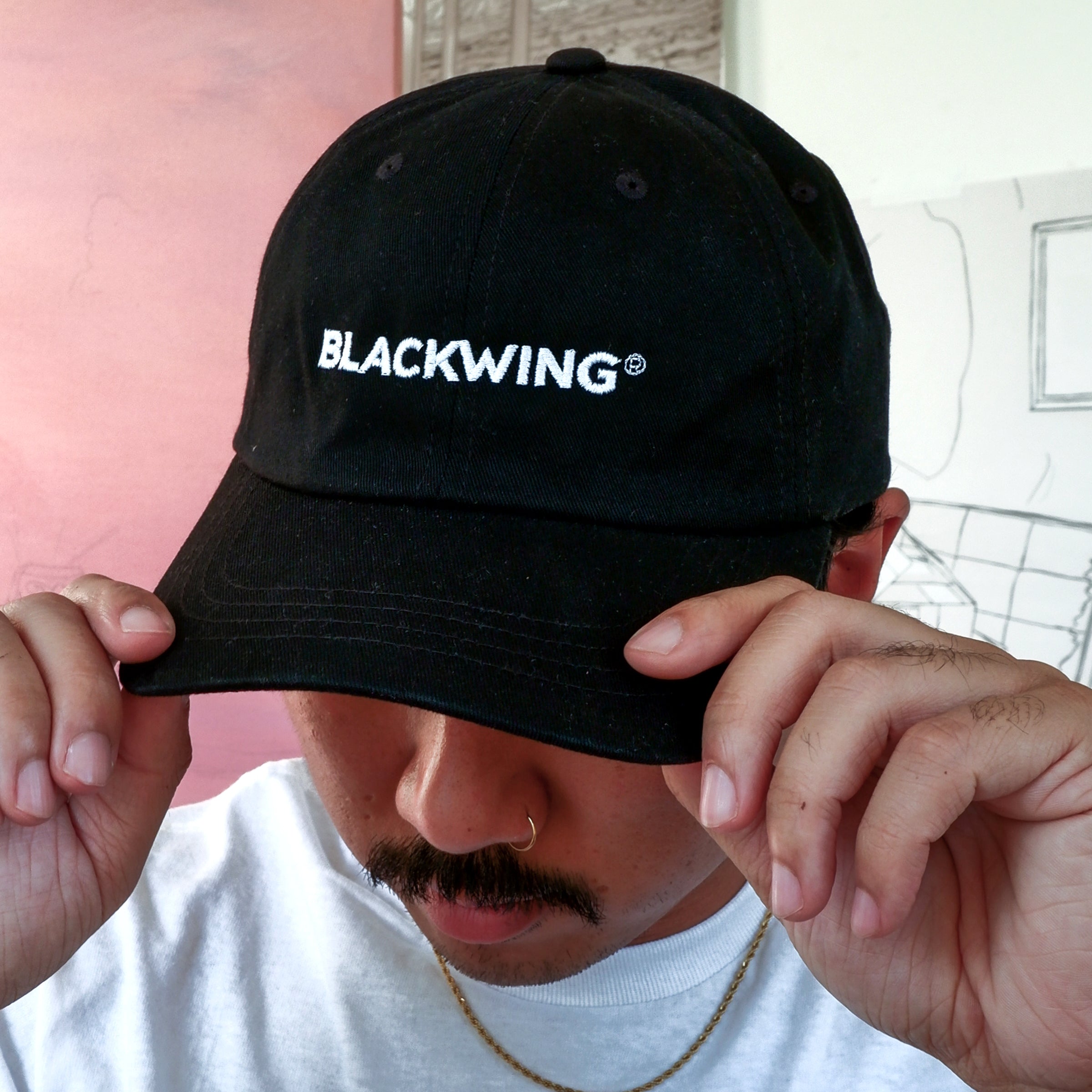 A man in a Blackwing Logo Hat is strolling down the street.