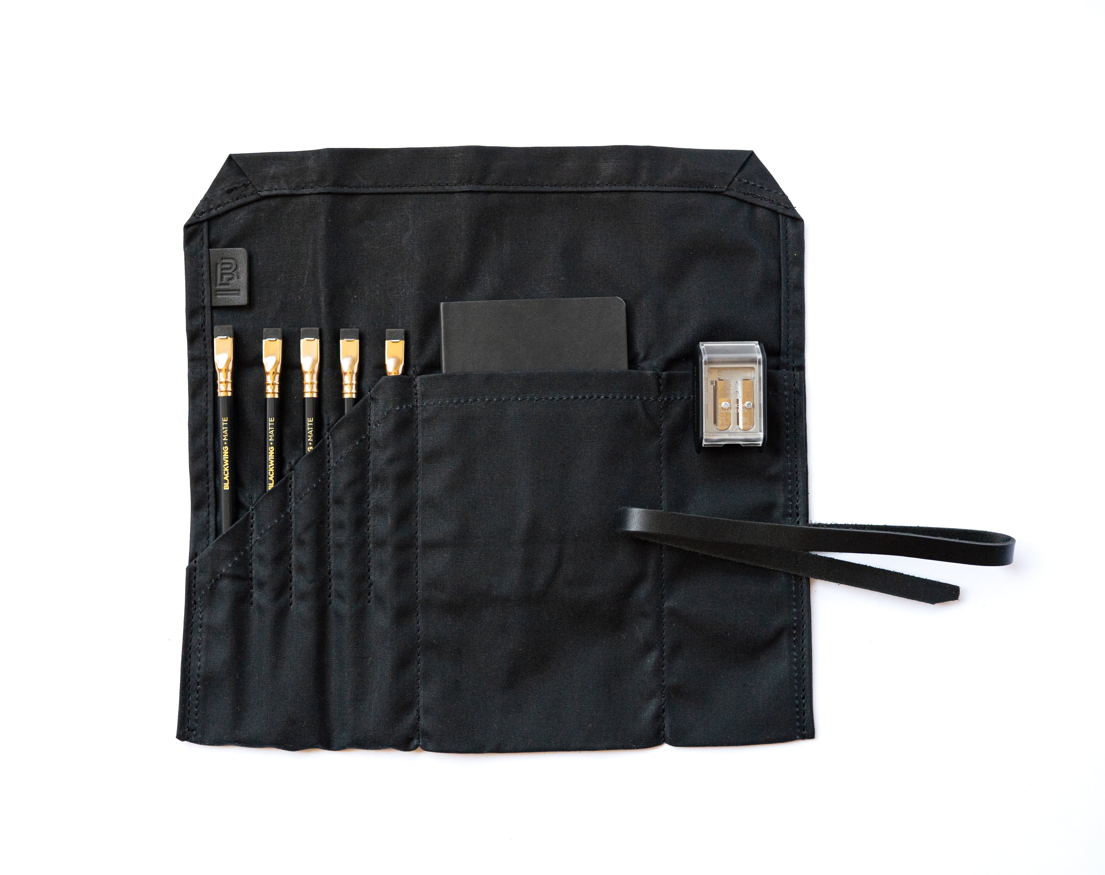 A Blackwing Pencil Roll with a set of brushes and Blackwing pencils, made from waxed canvas for durability and versatility.
