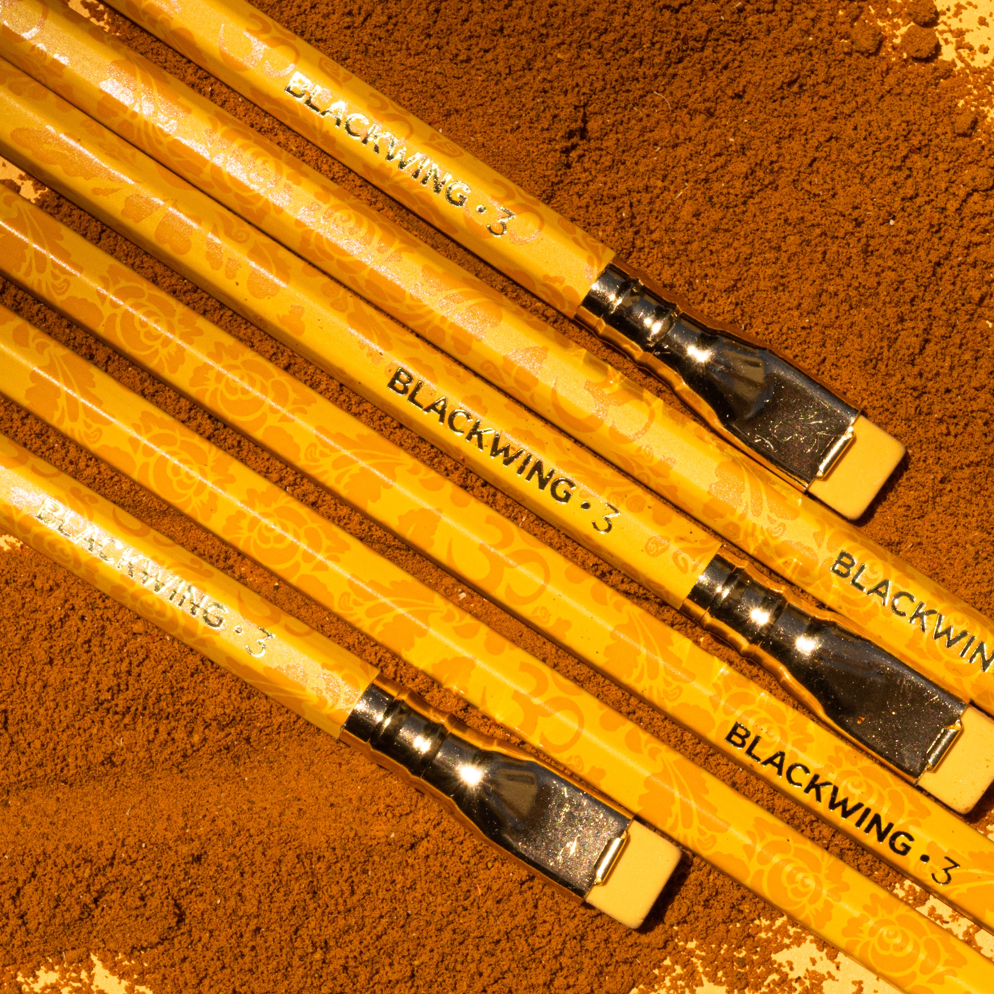 A group of Blackwing Volume 3 (Set of 12) pencils lay on top of a pile of sand.