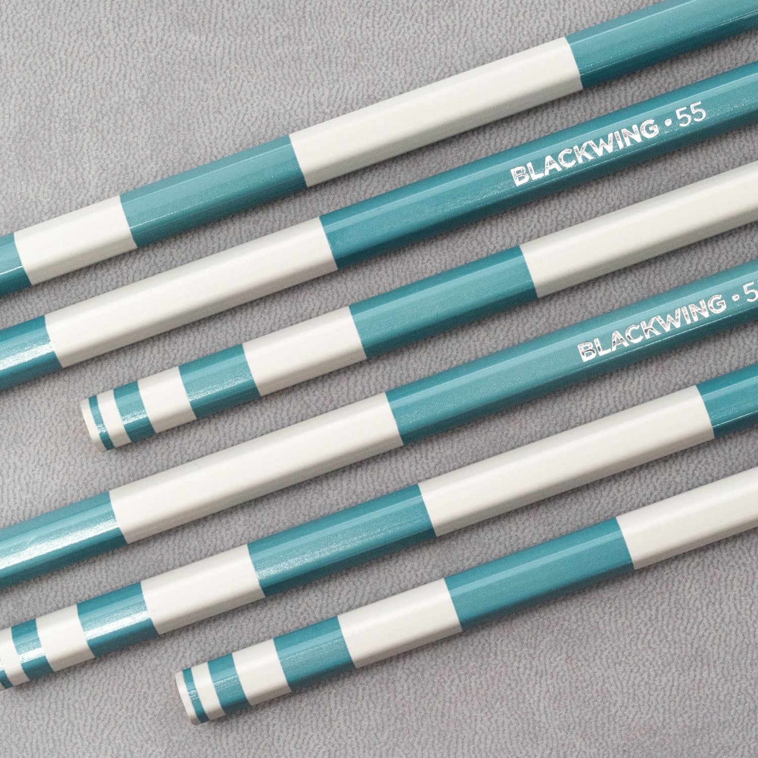 Five Blackwing Volume 55 (Set of 12) pencils on a gray surface, showcasing perfect symmetry.