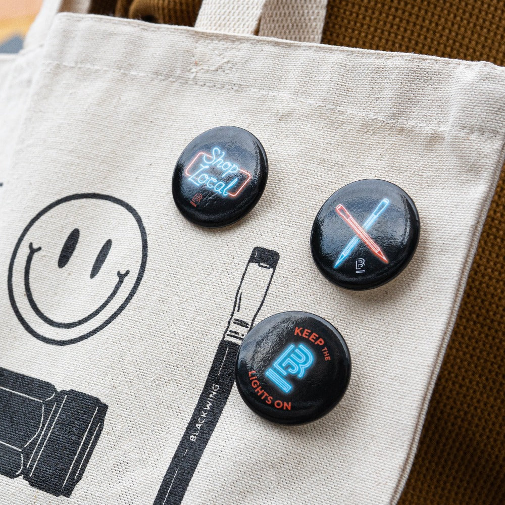 A tote bag with a smiley face and Blackwing Volume 6 Button Set is the perfect accessory for supporting independent businesses.
