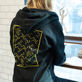 A woman in a Blackwing Sketch Zip-up Hooded Sweatshirt from the Winter 2019 collection sits at a table.