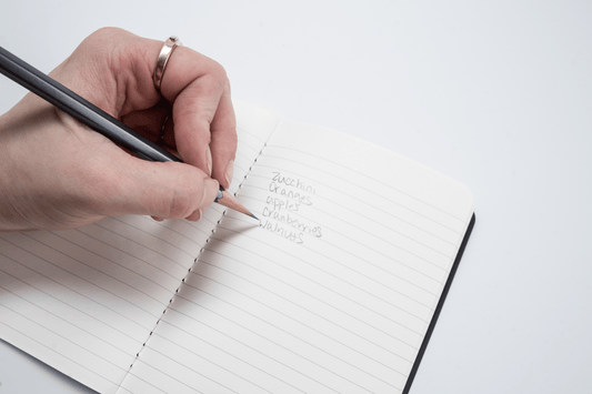 Person writing grocery list on paper with Blackwing pencil