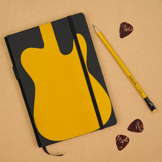 Blackwing x Fender notebook features the iconic Telecaster silhouette on its cover. One Butterscotch pencil and three Fender guitar picks surrounding the notebook on a tan background.