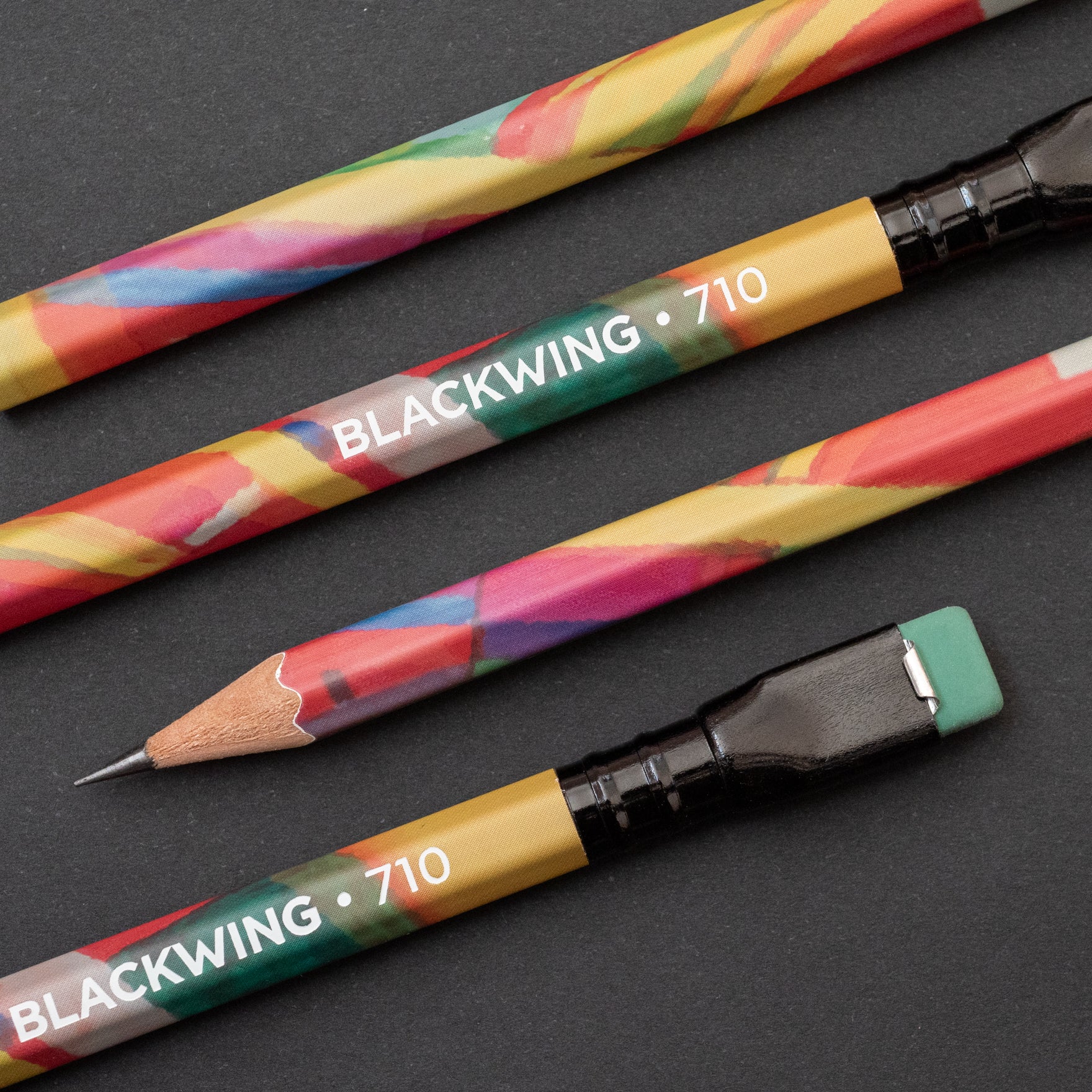 Three Blackwing Volume 710 (Set of 12) Grateful Dead pencils, two unsharpened and one sharpened with an exposed graphite tip, resting on a dark surface.