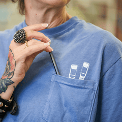 Person wearing a pocket tee with 2 white pencil graphics poking out of the chest pocket. A blackwing pencil is in the pocket.
