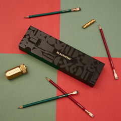 Blackwing Holiday Essentials Gift Set Box surrounded by the contents, including 2 green pencils, 2 red pencils, a gold sharpener, and a gold point guard on a red and green checkered background.