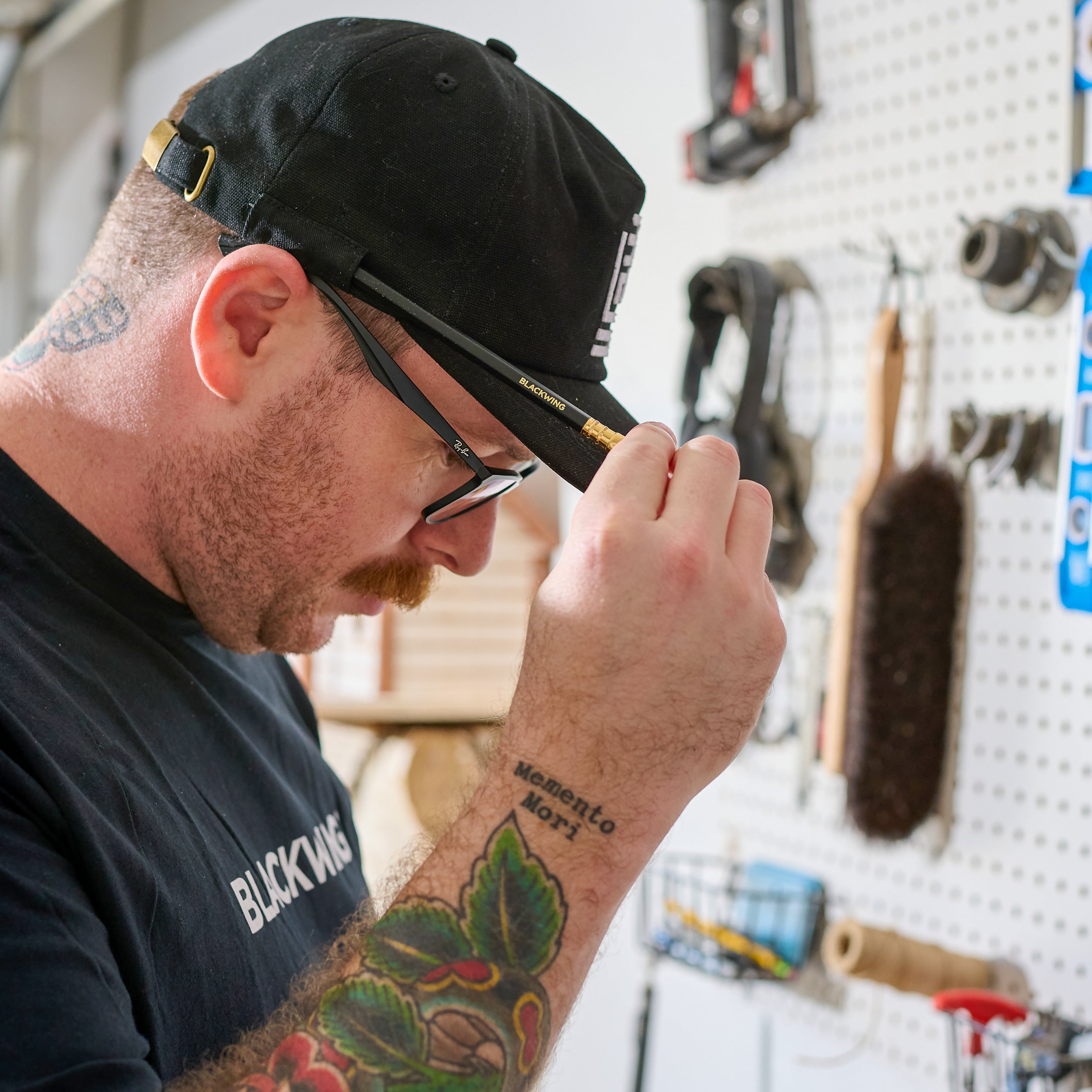Man in his workshop wearing a black cap with white Blackwing emblem embroidered on the front. The hat features a pencil loop on the side holding a Blackwing Matte pencil.