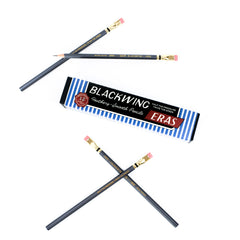 Twelve Blackwing drawing and sketching pencils with grey barrels, pink erasers, shown with their blue and white striped packaging box on a clean white background.