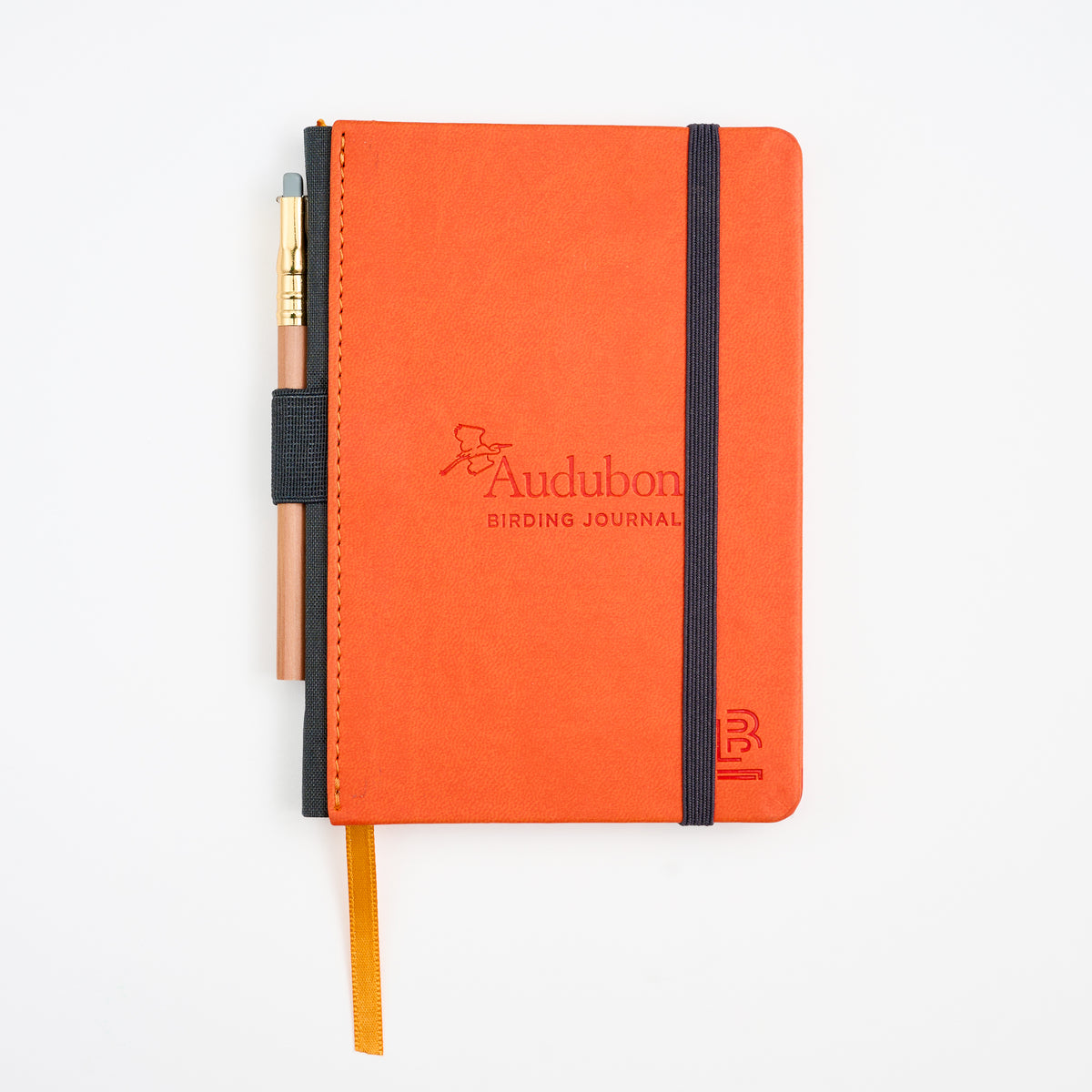 An orange Blackwing x Audubon birding journal with a black elastic closure band, a matching orange ribbon bookmark, and a pencil tucked into the side, photographed on a clean white background.