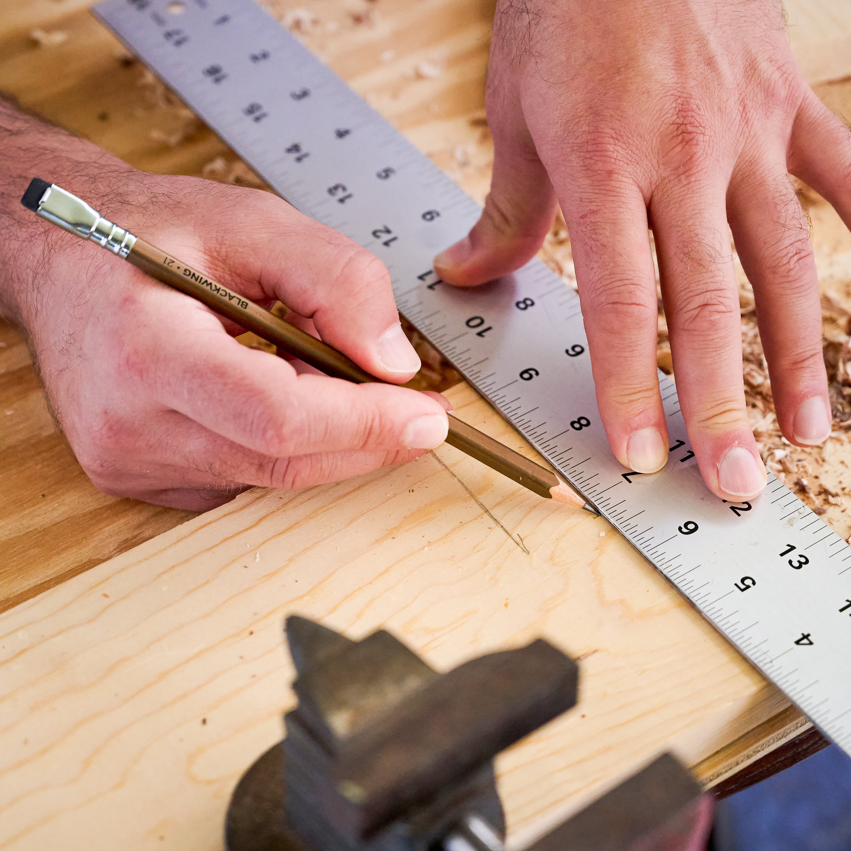 Person measuring wood with a metal ruler and marking with a Blackwing pencil