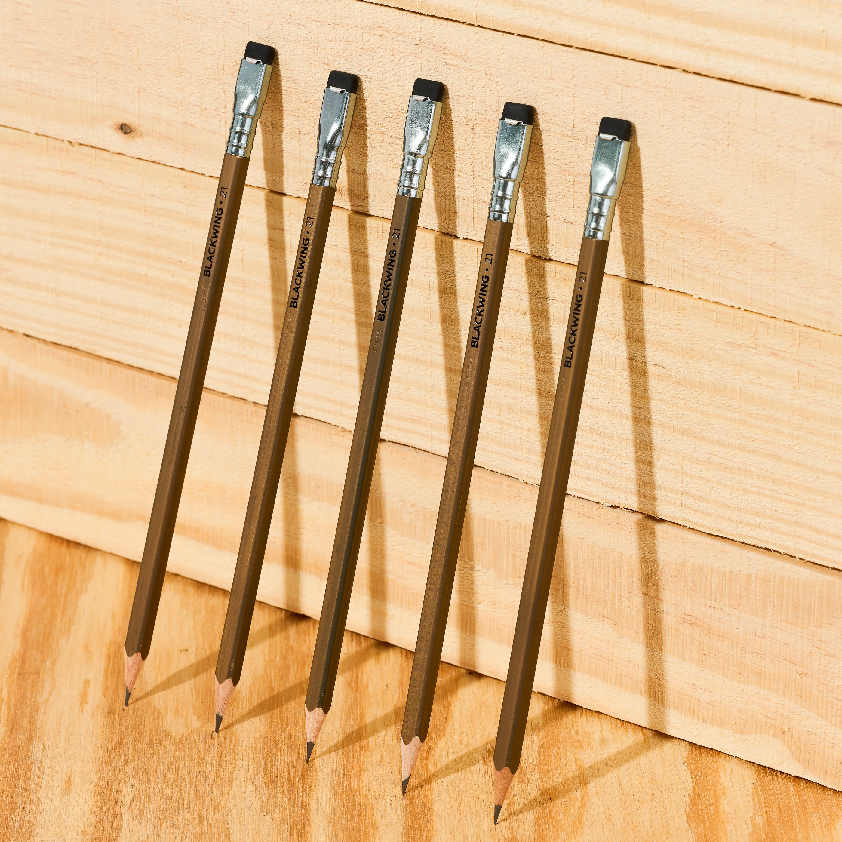 five Volume 21 Blackwing pencils against a wood wall. these pencils pay tribute to the craft of woodwokring and have a walnut stain barrel
