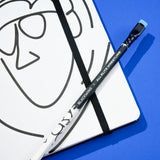 Blackwing x AEW "Freshly Squeezed" Orange Cassidy Notebook with a minimalist black line drawing of a face on a white cover with a matching pencil on top, all on a blue background