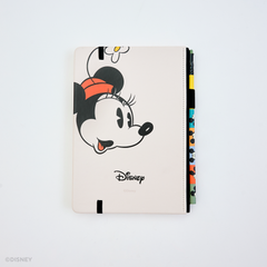 Back of a hardcover notebook featuring a large cartoon Minnie Mouse face, with the Disney logo printed below. The cover is an off-white color and is shown standing upright on a white background, with colorful matching pencil in the pencil holster on the right side.