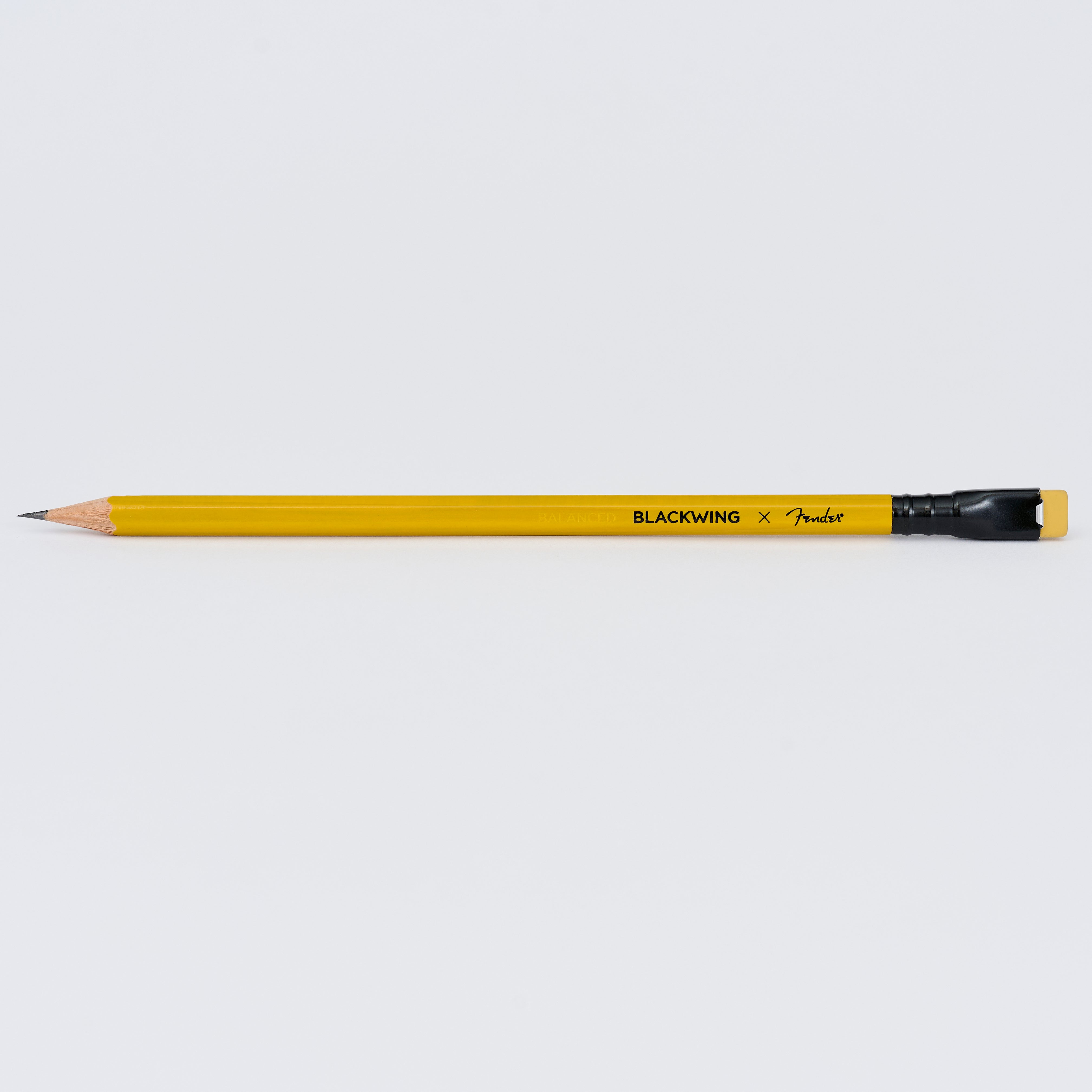 A sharpened yellow Blackwing x Fender pencil with a black ferrule and yellow eraser, shown horizontally against a light background.