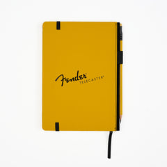 The back of a Fender Telecaster notebook in a signature yellow cover, featuring a black elastic closure band, a black pencil loop on the side with a matching pencil tucked inside, and the Fender Telecaster logo printed in black, set against a plain white background.