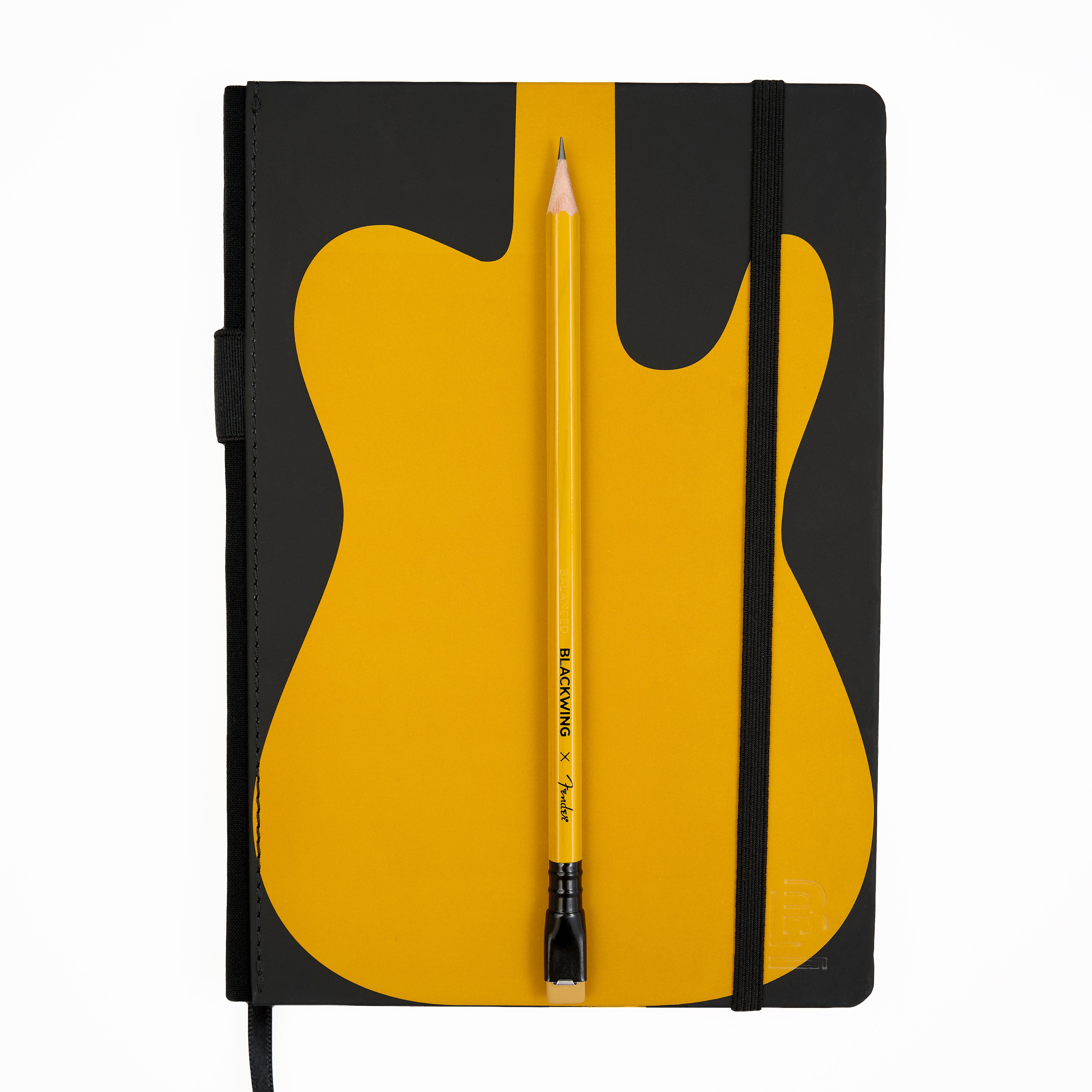 A hardcover notebook with a black cover featuring a large yellow guitar-body graphic, shown closed with a black elastic band. A yellow pencil is placed vertically in the center of the cover with black imprint reading 'BLACKWING x Fender'.