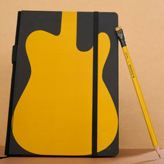 A notebook with a black cover featuring a large yellow guitar-shaped graphic to symbolize the Fender Butterscotch guitar, shown standing upright next to a black and yellow pencil on a beige background.