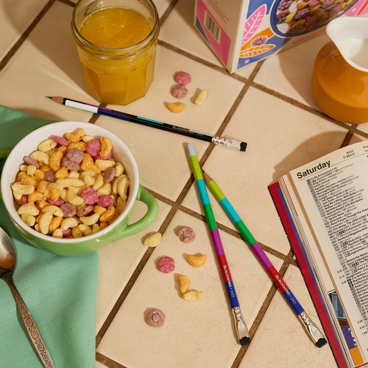blackwing colorful graphite pencils on a kitchen counter next to cereal bowl, orange juice, and tv guide