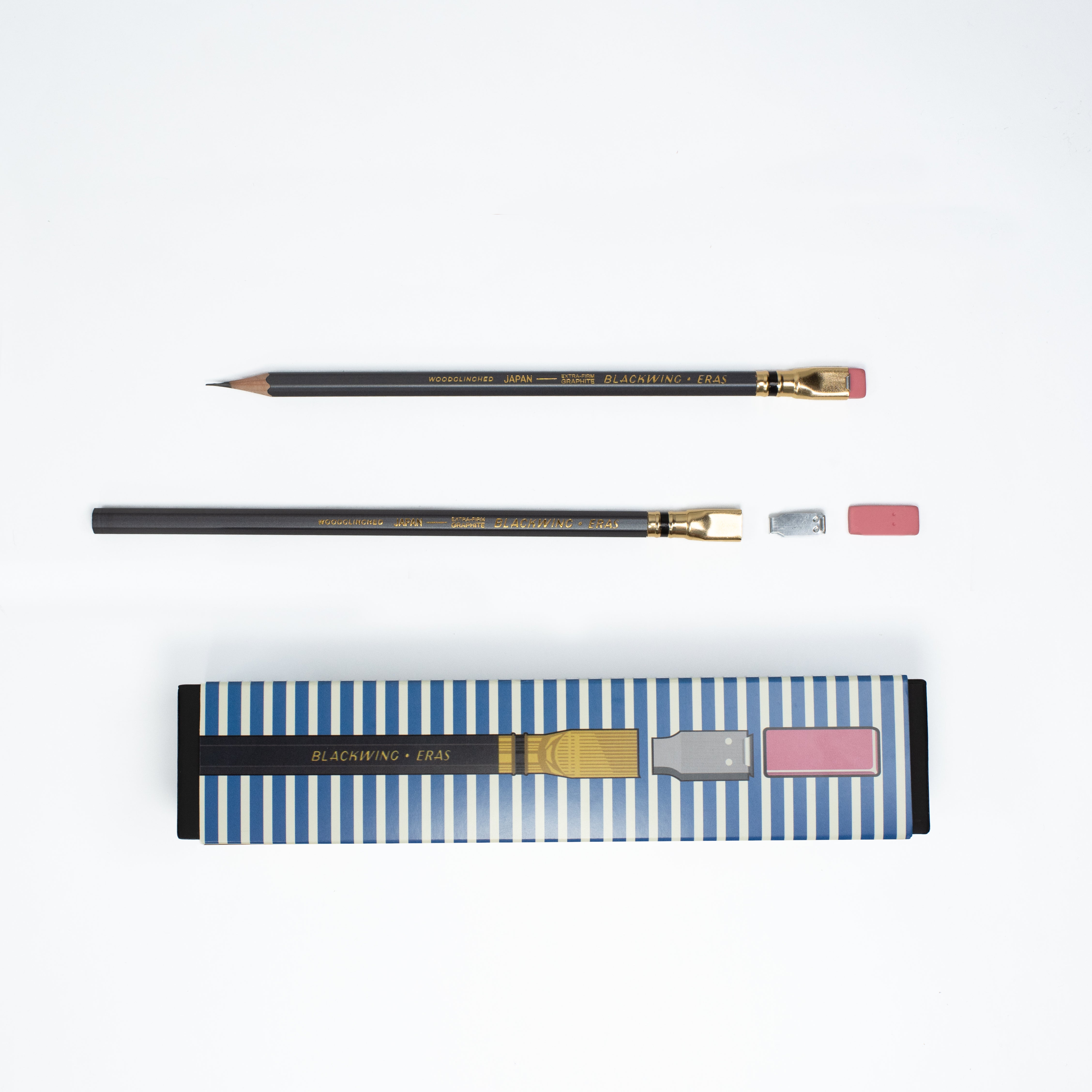 Two dark grey pencils with gold ferrules and pink erasers, shown alongside their blue-and-white striped packaging on a clean white background.