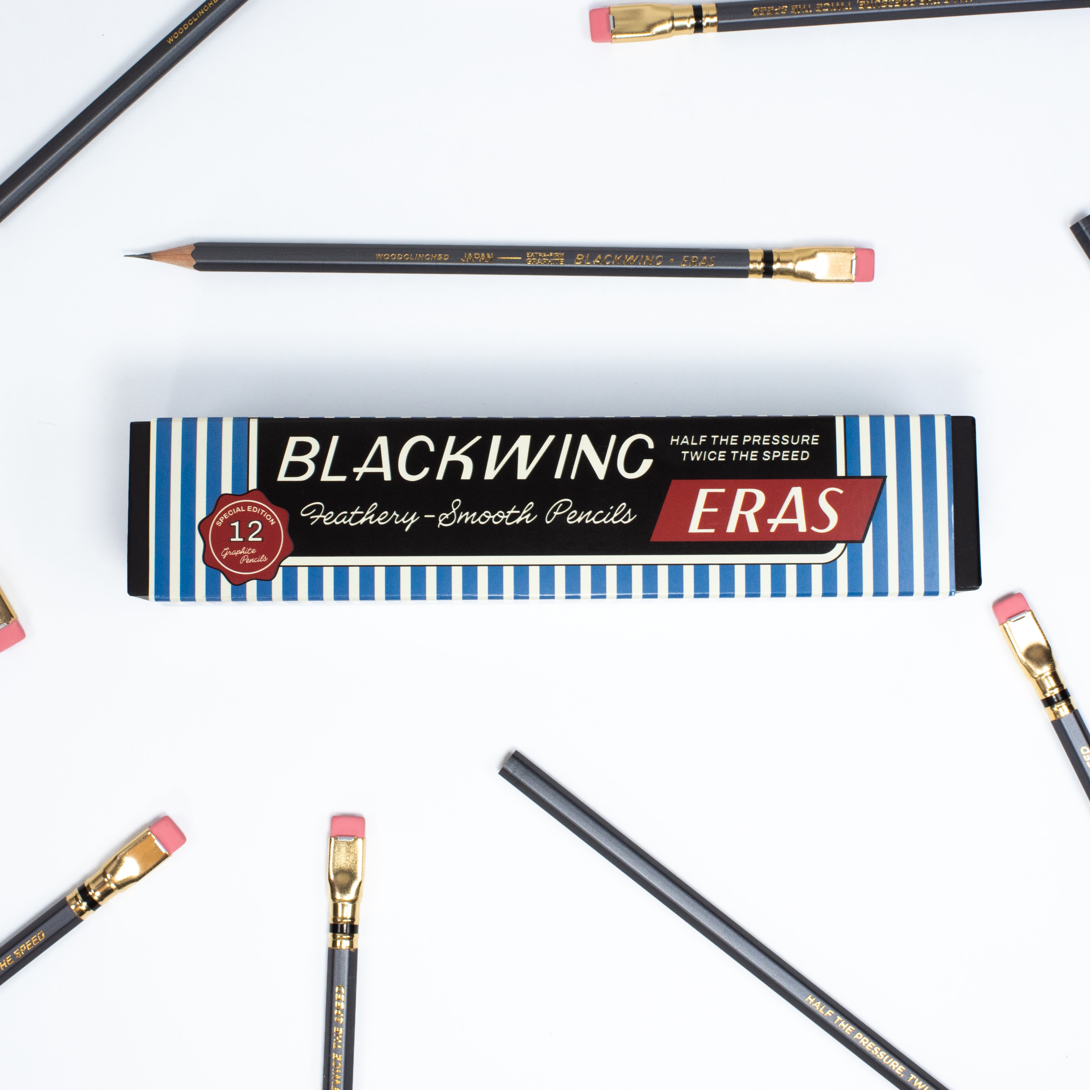 A flat-lay of a Blackwing Eras graphite smooth pencil box on a white background, surrounded by several black pencils with gold ferrules and pink erasers.
