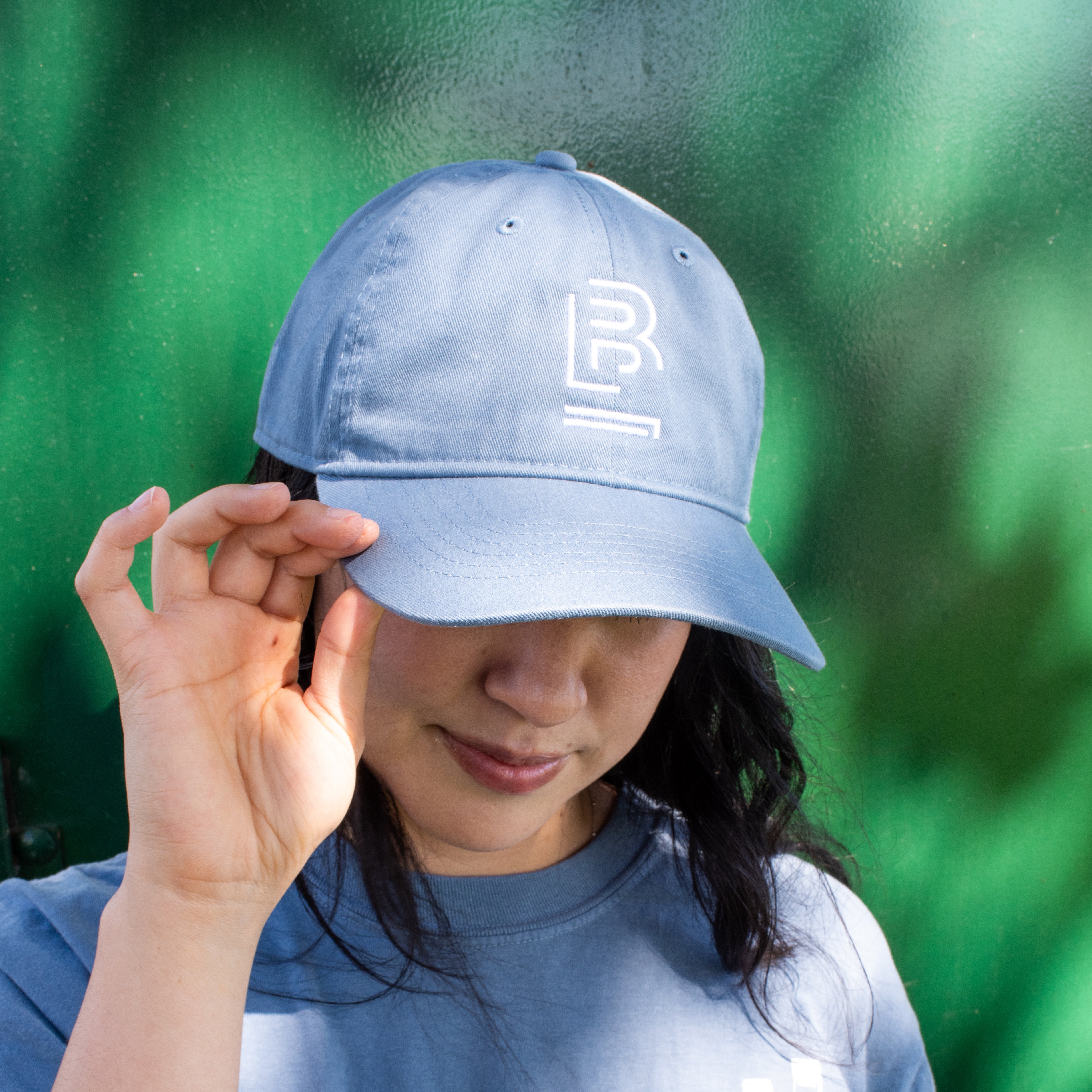 woman wearing a blue cotton hat and blue t-shirt against a green background