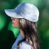 side profile of a woman wearing a blue baseball cap and blue t-shirt against a green background