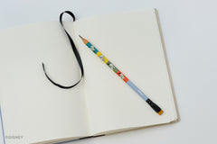 A Blackwing pencil with colorful Donald Duck illustrations rests on an open blank notebook with a black ribbon bookmark, shot from a top-down angle on a clean white background.