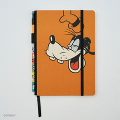An orange hardcover notebook by Blackwing featuring a cartoon Goofy illustration on the front, with a black elastic closure band and a matching black ribbon bookmark. A colorblock pencil with Goofy graphics is tucked into the left side.