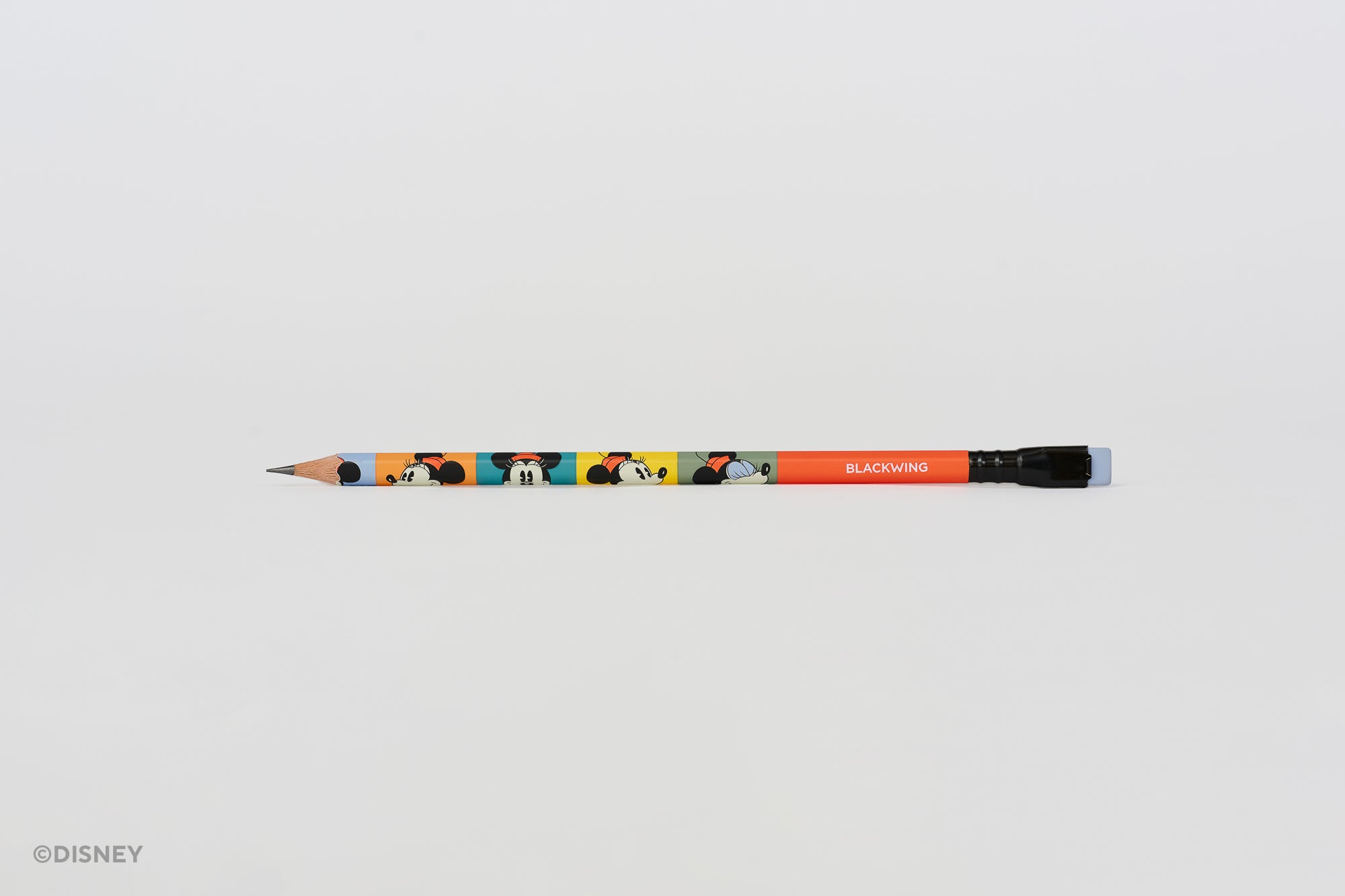 A Disney branded Blackwing pencil with colorful Minnie Mouse illustrations and a red-orange barrel, shown horizontally on a plain light gray background.