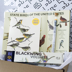 Blackwing Vol. 458 Subscription Box open showing the contents which includes a box of Vol. 458 pencils, Issue 002 of the zine, State Bird Map, and archive pencil. All have illustrations of various birds.