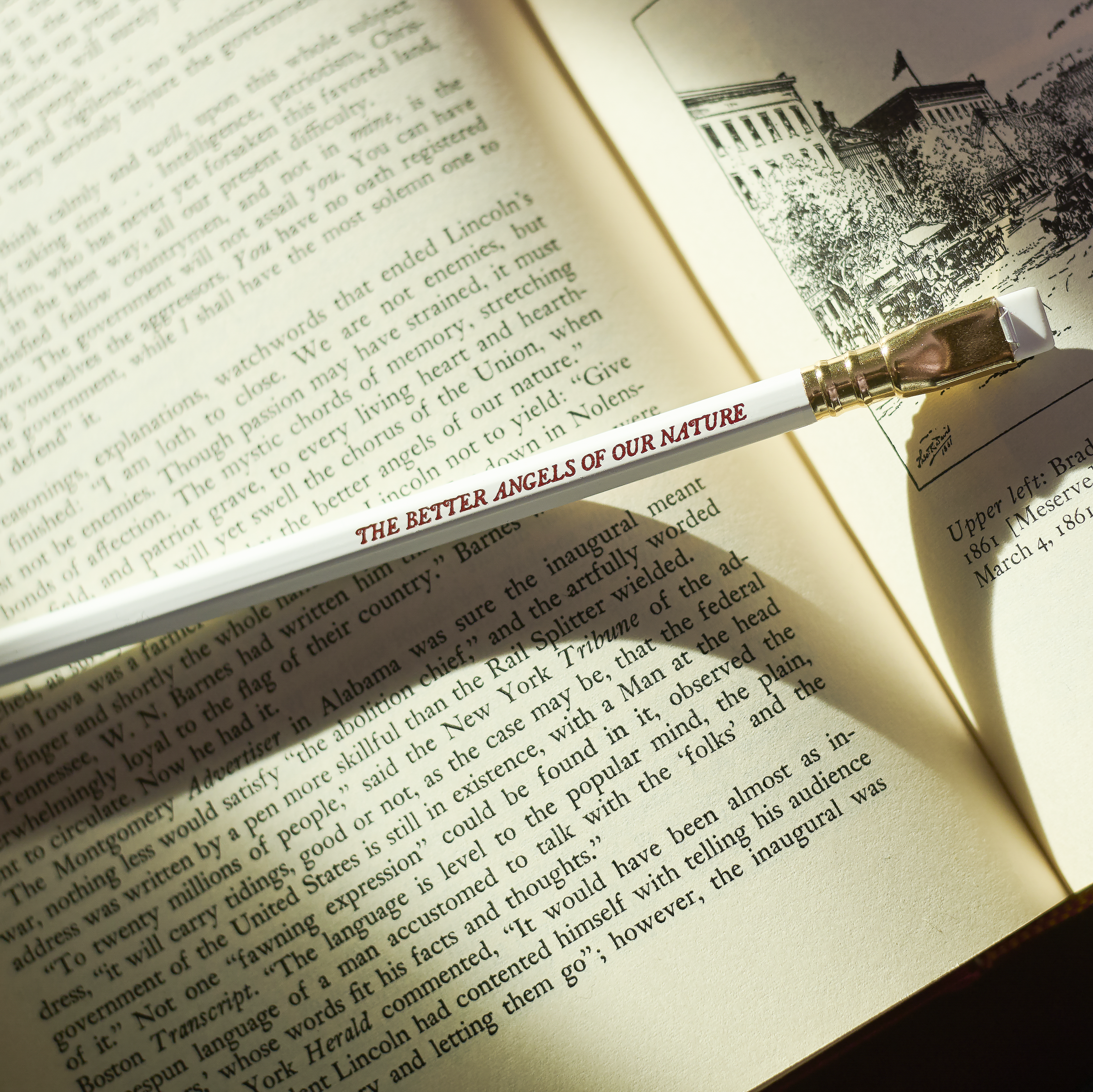 white pencil with red imprint that says 'THE BETTER ANGELS OF OUR NATURE' on top of an open book