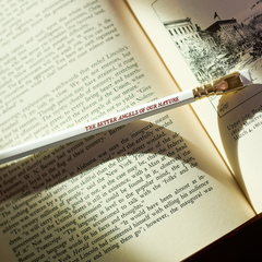 white pencil with red imprint that says 'THE BETTER ANGELS OF OUR NATURE' on top of an open book
