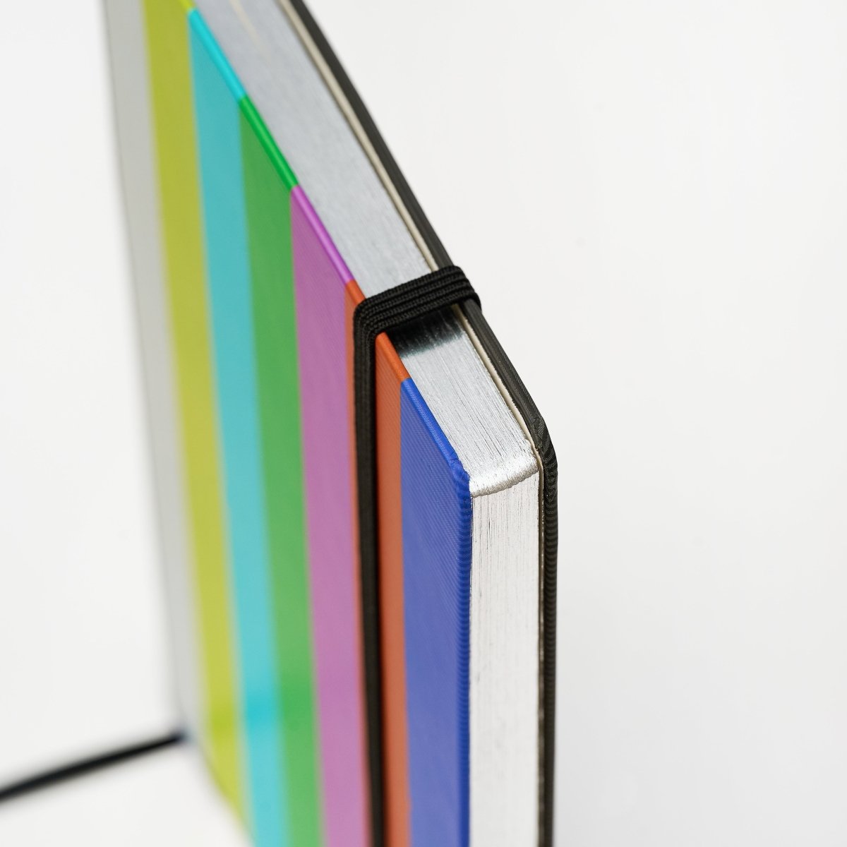 Close-up of a notebook with colorful cover and a black elastic band keeping it closed on a white background