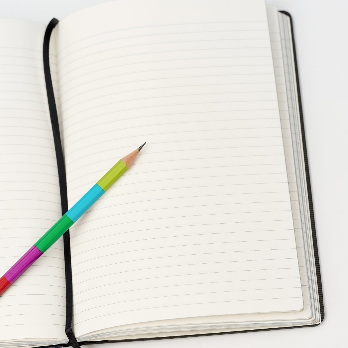 lined notebook laying open with a sharpened colorblock pencil on top.