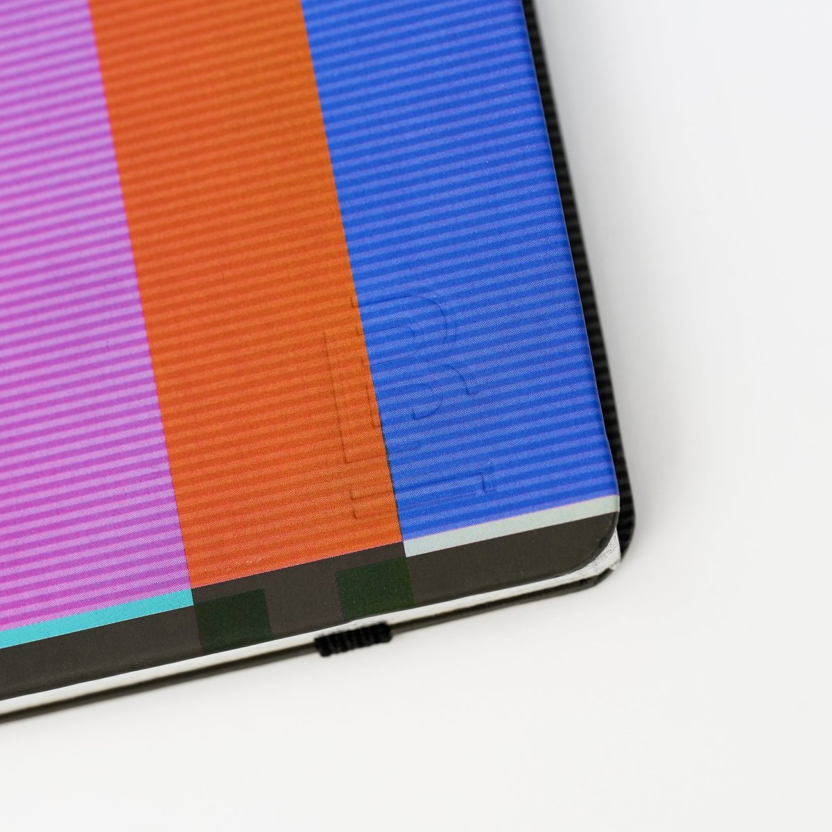 close-up of colorful striped notebook with a 'B' emblem in bottom-right corner, on a white background
